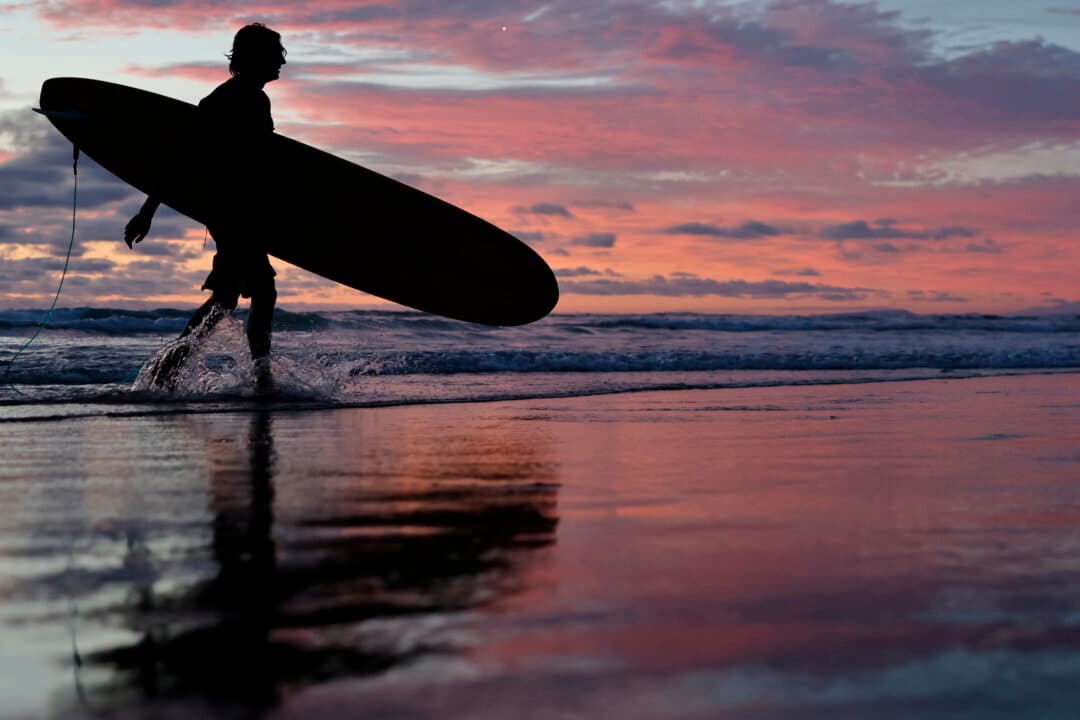 A surfer walks out of the Pacific Ocean as the sun sets in the La Jolla neighborhood near Scripps Pier in San Diego on Aug. 13, 2026. (Mario Tama/Getty Images)