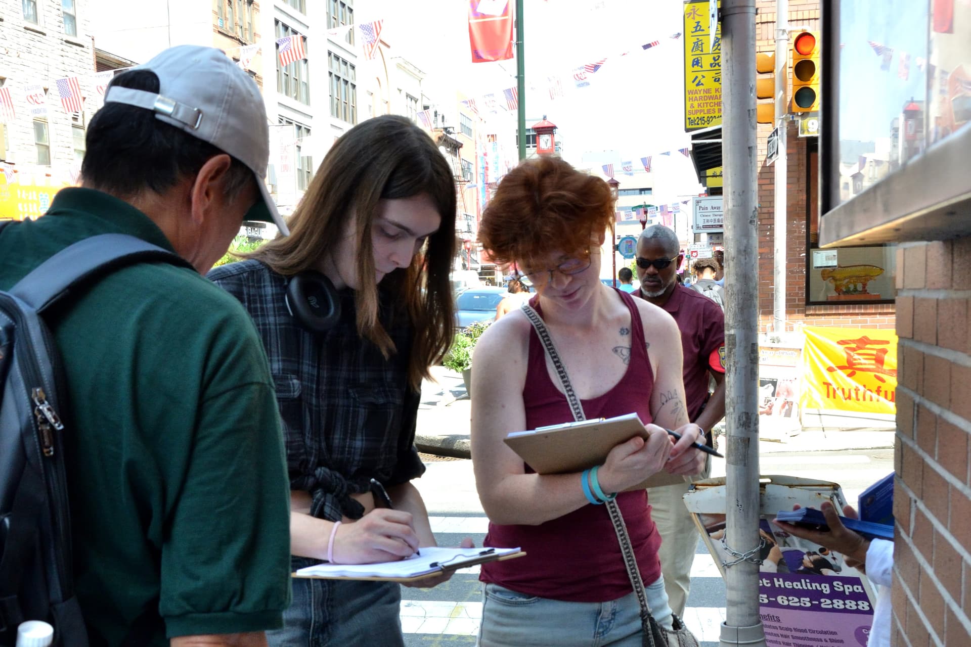 Security professional Amy (C) and artist Mula (R) sign the petition for S. 4009 in Philadelphia on Aug. 15, 2026. (Frank Liang/The Epoch Times)