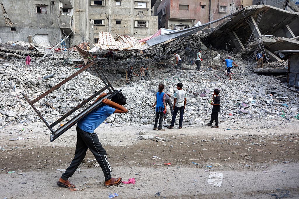 A boy carries a table on his back past salvage workers scrapping the rubble of a building that was destroyed during Israel's war against the Hamas terrorist group in the Gaza Strip, to use the recycled remains in the future, in Gaza City, Gaza Strip, on Aug. 16, 2026. (Omar Al-Qattaa/AFP via Getty Images)