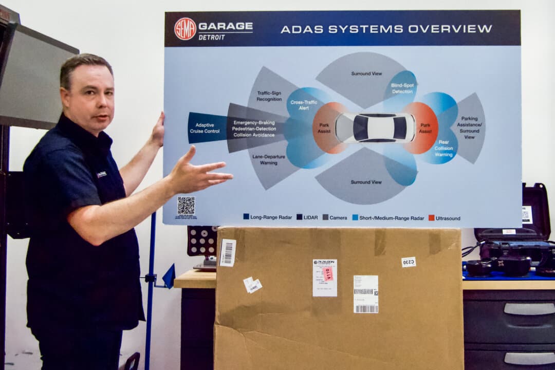 Ben Kaminsky, general manager of SEMA's Detroit Garage, displays a sign illustrating sensors used in vehicles' automatic driver assist systems at the organization's facility in Plymouth, Michigan, on July 28, 2026. (Travis Gillmore/The Epoch Times)