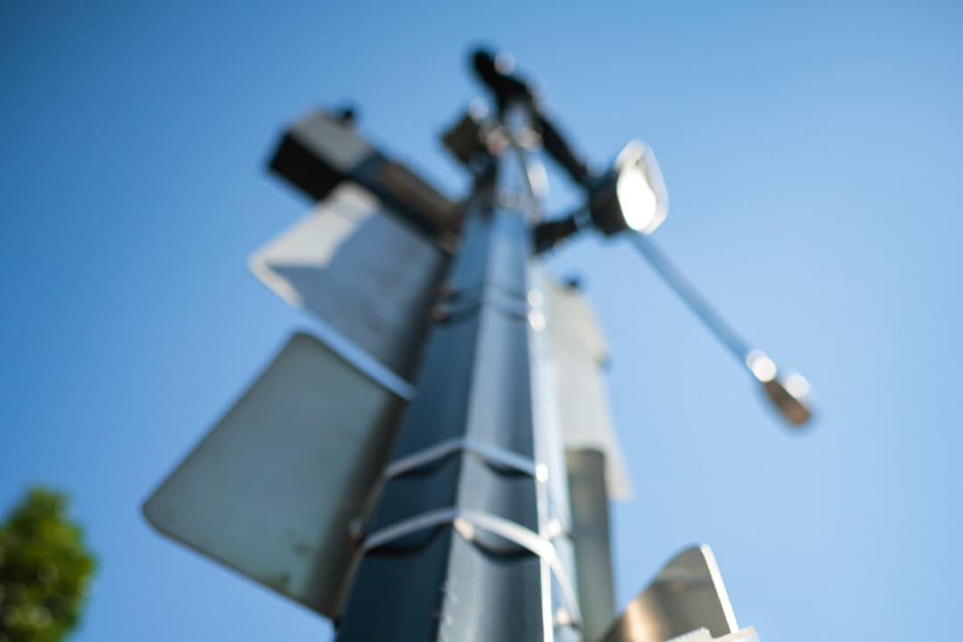 (Left) A Flock Safety automatic license plate reader camera is attached to a traffic light pole along 16th Street Northwest in Washington on Aug. 19, 2026. (Right) A sign taped to a street light points to a Flock brand automatic license plate reader camera along 16th Street Northwest in Washington on Aug. 19, 2026. (Chip Somodevilla/Getty Images)