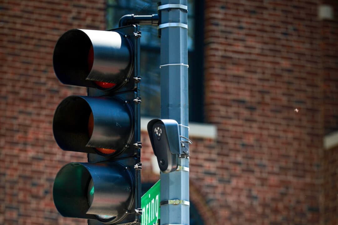 (Left) A Flock Safety automatic license plate reader camera is attached to a traffic light pole along 16th Street Northwest in Washington on Aug. 19, 2026. (Right) A sign taped to a street light points to a Flock brand automatic license plate reader camera along 16th Street Northwest in Washington on Aug. 19, 2026. (Chip Somodevilla/Getty Images)