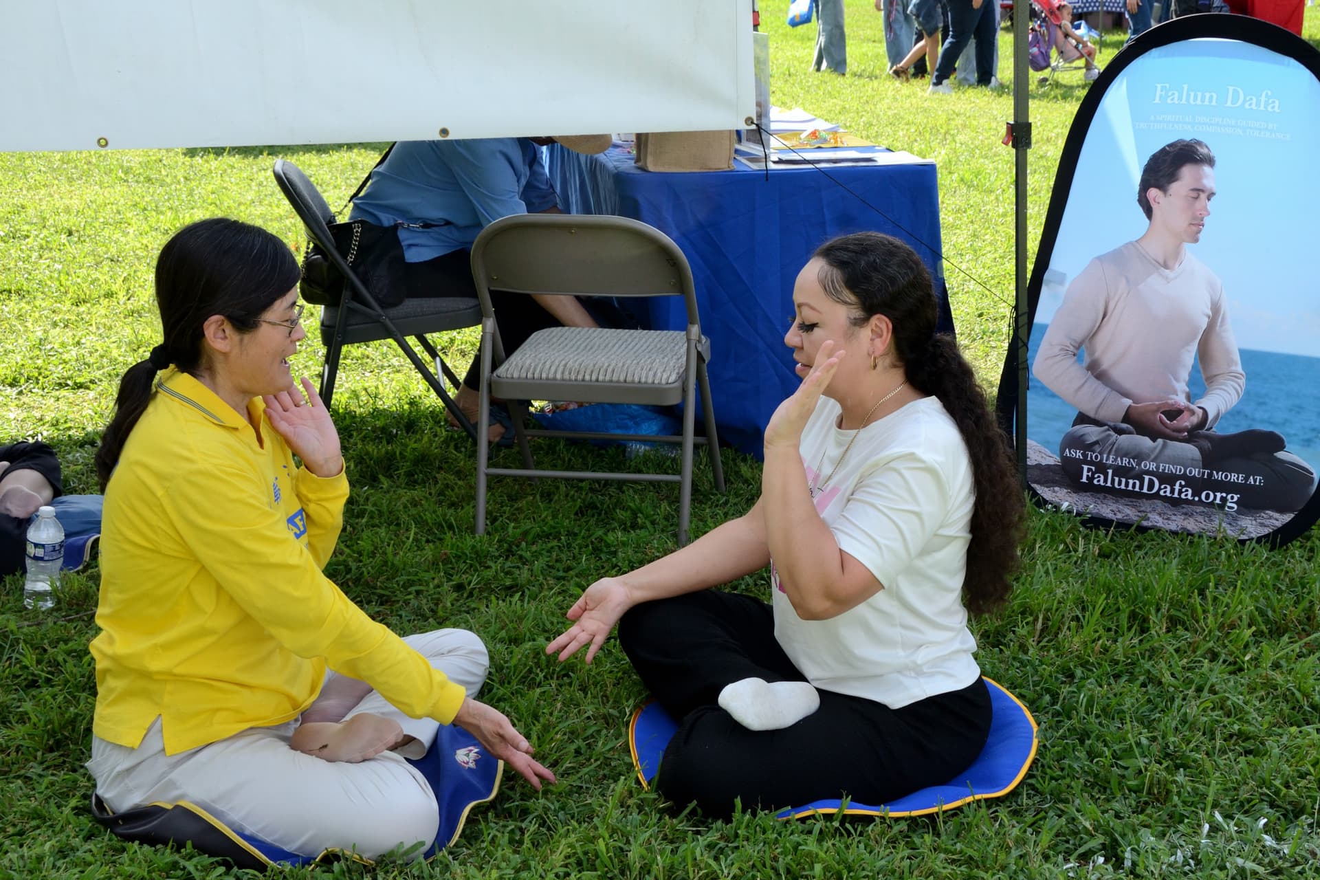 Vanessa Alstos (R), an event vendor, learns Falun Gong exercises at the 4th annual Baila Con Dover Latin Festival on Aug. 29, 2026. (Frank Liang/The Epoch Times)