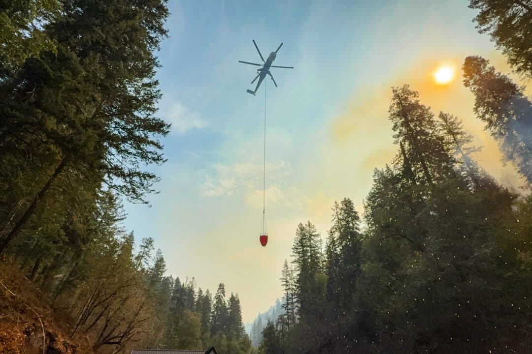 A helicopter refills a bucket of water from Oregon's Mill Creek for firefighting operations against the Paradise fire in northeast Oregon on Aug. 26, 2026. (T.J. Muscaro/The Epoch Times)