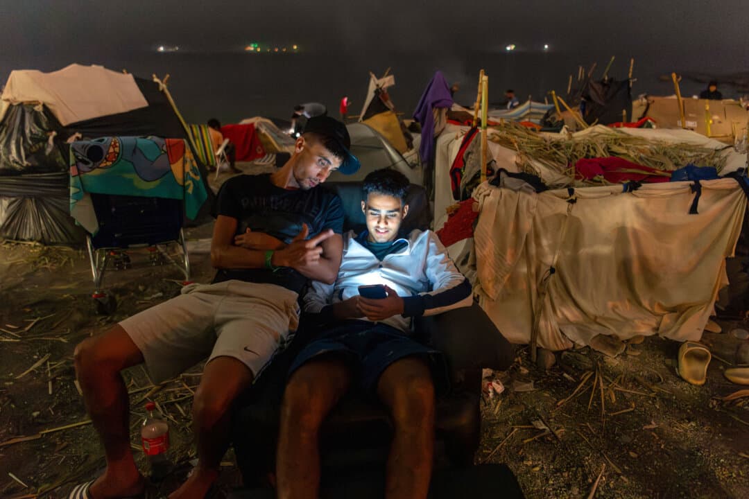 Two migrants use a smartphone as they spend the night near makeshift shelters on El Trampolin beach, in Ceuta, Spain, on Sept. 1, 2026. Spanish authorities are investigating claims that Moroccan security forces were responsible for a mass migrant entry into the enclave in July. (Antonio Sempere/AFP via Getty Images)