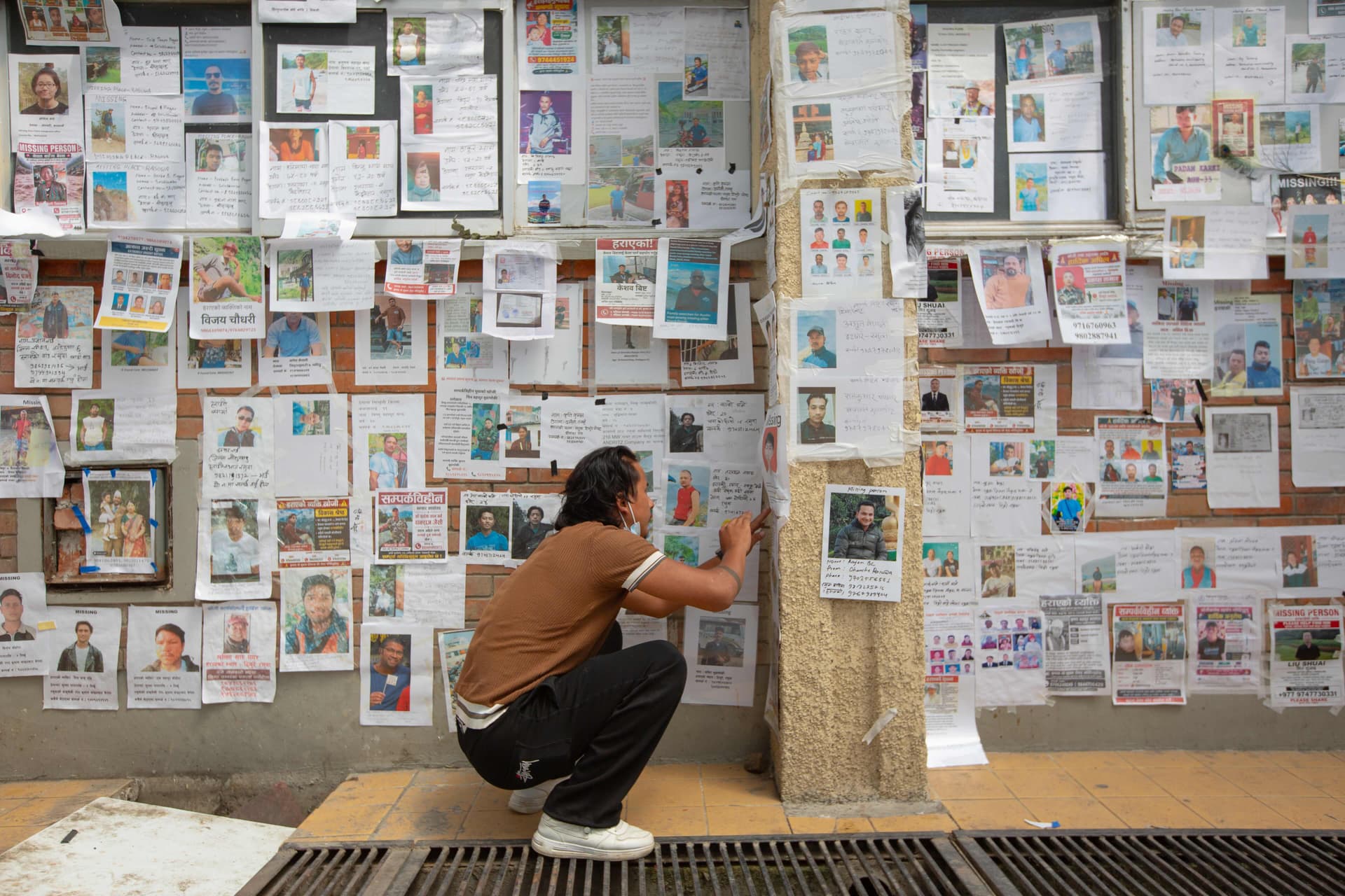 A man affixes a photo of a missing relative on a wall covered with photographs of people reported missing after the recent floods in the Himalayan valley along the Nepal–Tibet border, inside the Tribhuvan University Teaching Hospital in Kathmandu, Nepal, on Sept. 8, 2026. (Abhishek Chinnappa/Getty Images)