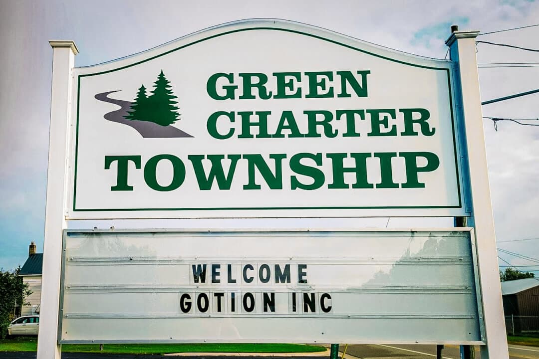 (Top) Manteno residents opposed to a Gotion battery plant demonstrate outside the Kankakee County Courthouse in Kankakee, Ill., on Jan. 14, 2025. (Bottom Left) A sign states “Welcome Gotion Inc” in Green Charter Township, Mich., in this file photo. Residents successfully stopped the Chinese battery maker from building a plant in the rural community. (Bottom Right) An overhead sign signifies downtown Manteno, Ill., on Sept. 3, 2026. (Courtesy of Amanda Piker, Courtesy of Jim Chapman, Nathaniel Smith for The Epoch Times)