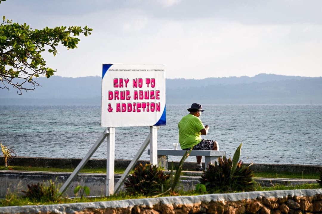 A man sits near a sign posted on a beach in Koror, Palau, on Aug. 31, 2026. The sign reflects the country's efforts to halt a growing drug problem. (Saeed Khan/AFP via Getty Images)
