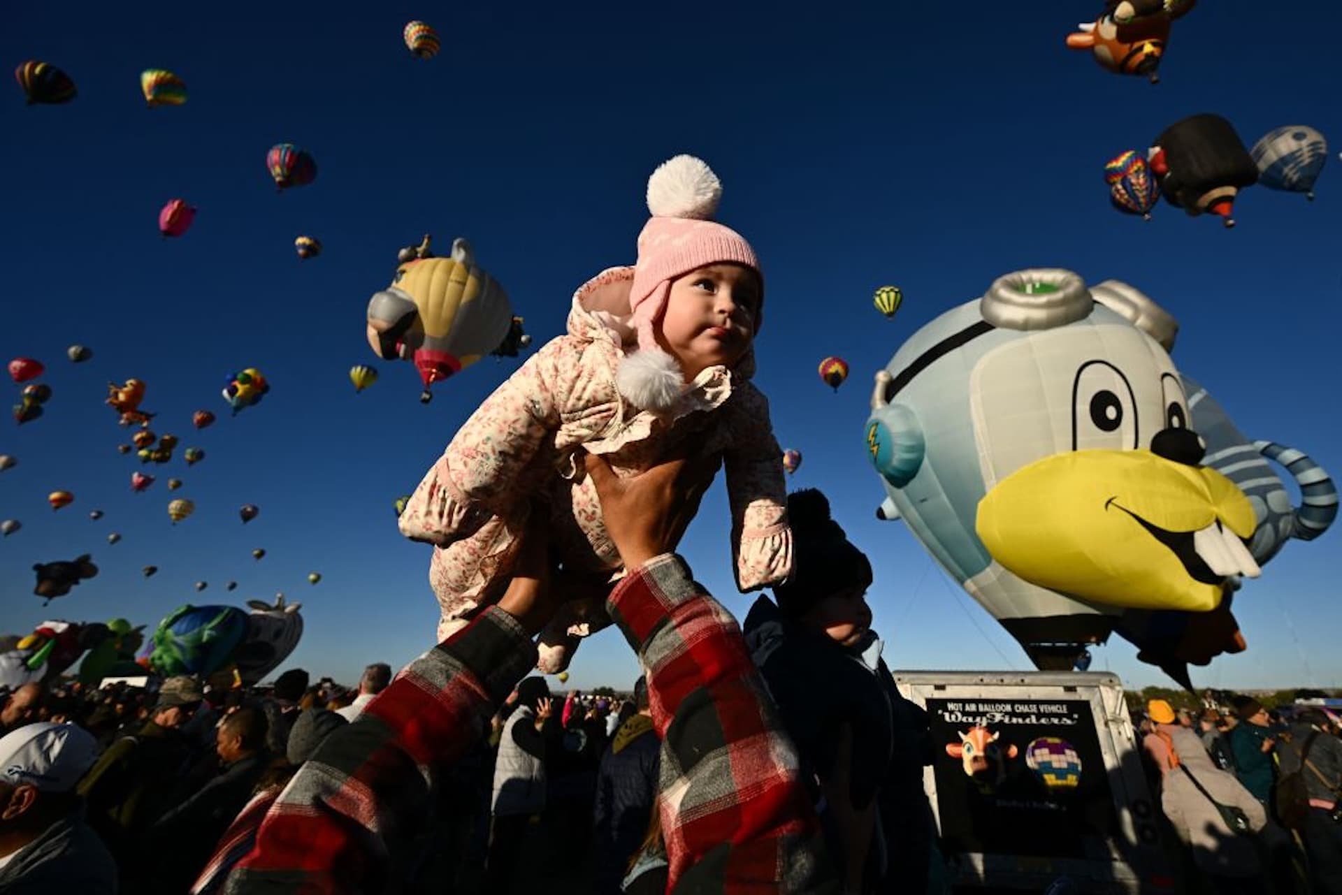 Clarissa is lifted into the air by her father as hot air balloons take flight at sunrise during the Albuquerque International Balloon Fiesta in Albuquerque, New Mexico on October 13, 2023. (Photo by Patrick T. Fallon / AFP)