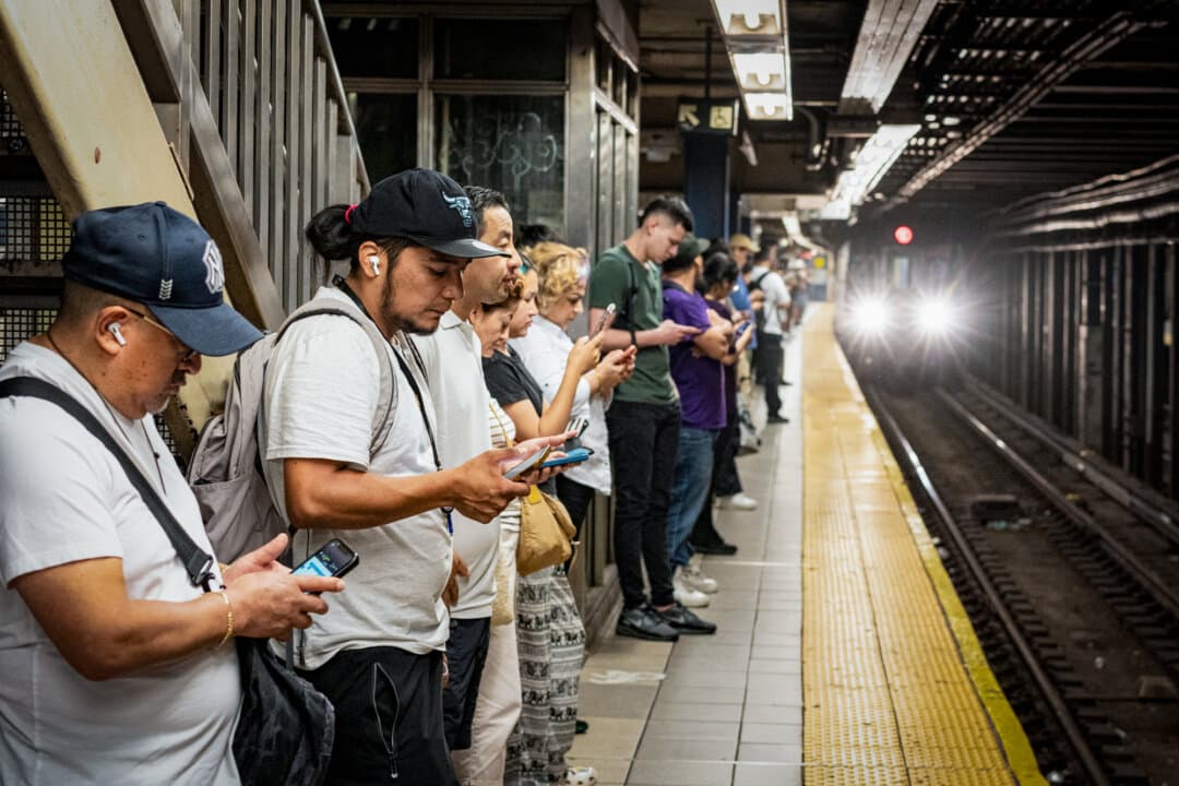 Commuters engage with their phones as they await the subway in New York City on June 28, 2024. Today's Christian influencers are reaching millions of believers through apps such as Youtube and TikTok. (Samira Bouaou/The Epoch Times)