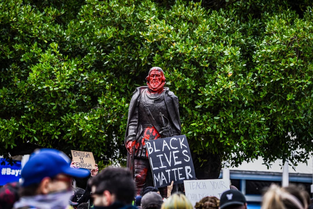 (Clockwise from Top Left) Protesters surround the Robert E. Lee statue in Richmond, Va., on June 23, 2020. A demonstrator hangs a banner from a statue of Union Army Gen. Harrison Gray Otis in MacArthur Park in Los Angeles during a May Day demonstration on May 1, 2026. Protesters climb on a statue of Abraham Lincoln during a “No Kings” protest in San Francisco on June 14, 2025. Protesters gather around a vandalized statue of Ponce de Leon in downtown Miami on June 12, 2020. A wave of backlash against figures like Christopher Columbus, Juan Ponce de León, and famous U.S. presidents portrays them as symbols of oppression or white privilege. (Eze Amos/Getty Images, Justin Sullivan/Getty Images, Benjamin Fanjoy/AP Photo, Chandan Khanna/AFP via Getty Images)