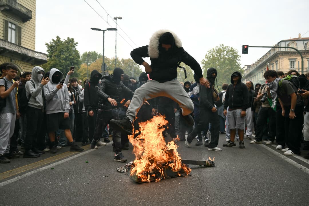 A student jumps over a burning cardboard tank during "No Meloni Day," a nationwide day of marches, in Turin, Italy, on Oct. 16, 2026. Demonstrators protested the cost of living, a proposed school decree, and the condition of school buildings, and called for increased education funding. The mobilization was inspired by protests in France and Spain. (Marco Bertorello/AFP via Getty Images)