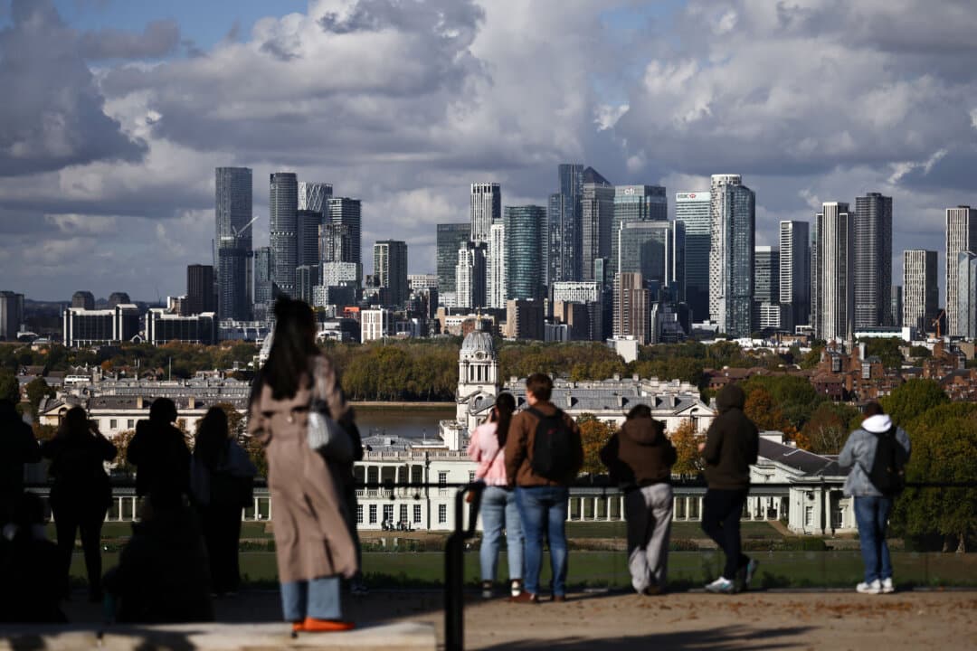 People look toward the Canary Wharf financial and business district from Greenwich Park in southeast London on Oct. 16, 2026. Britain's economy grew unexpectedly in August, according to official data, offering a boost to Finance Minister John Healey ahead of the government's budget update later this month. (Henry Nicholls/AFP via Getty Images)