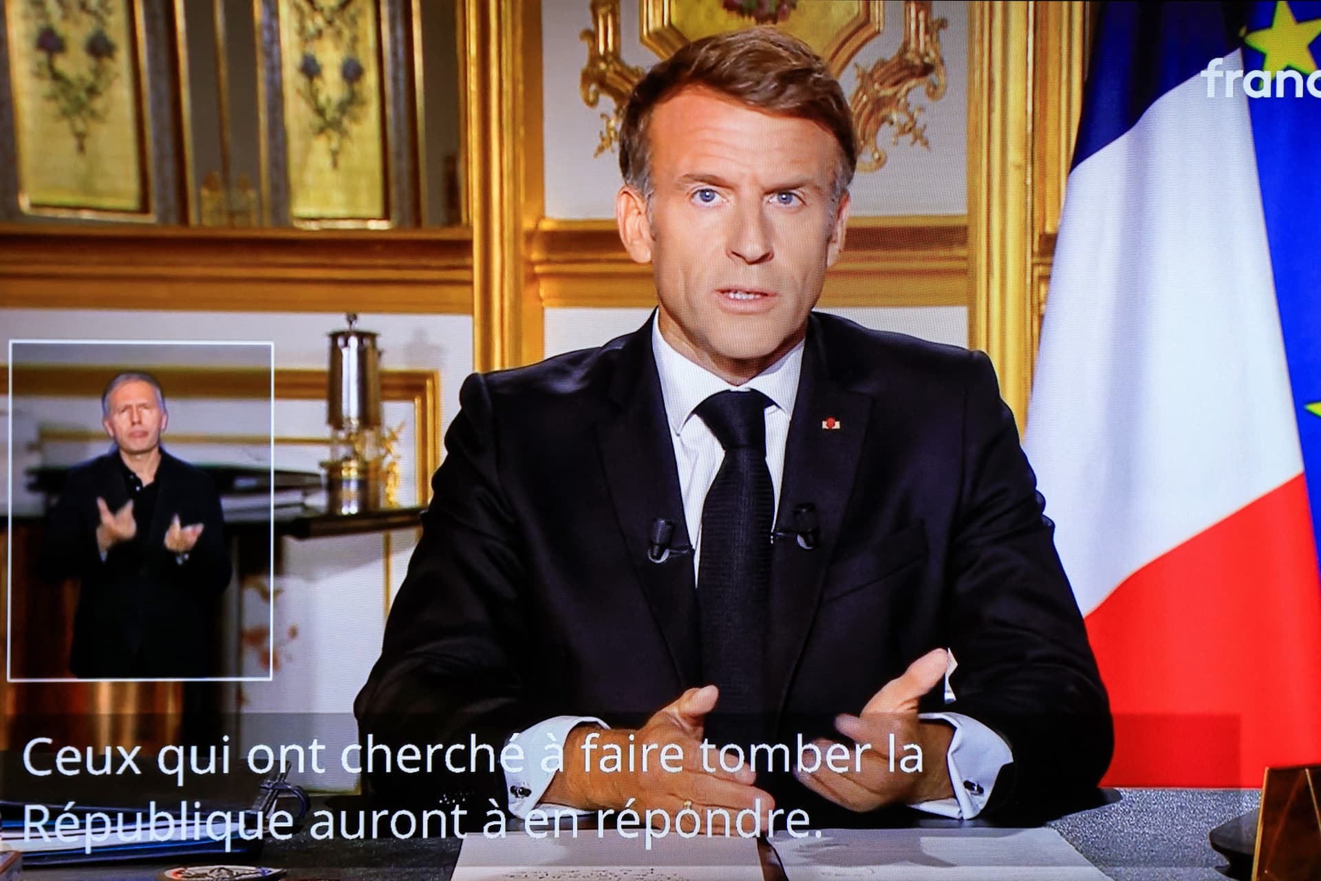 A television monitor broadcasts France's President Emmanuel Macron giving a speech from the Elysee Presidential Palace and subtitles reading, “Those who tried to bring down the Republic will have to answer for it,” the day after riots and looting on the sidelines of nationwide protests, in Paris on Oct. 18, 2026. (Ludovic Marin/AFP via Getty Images)